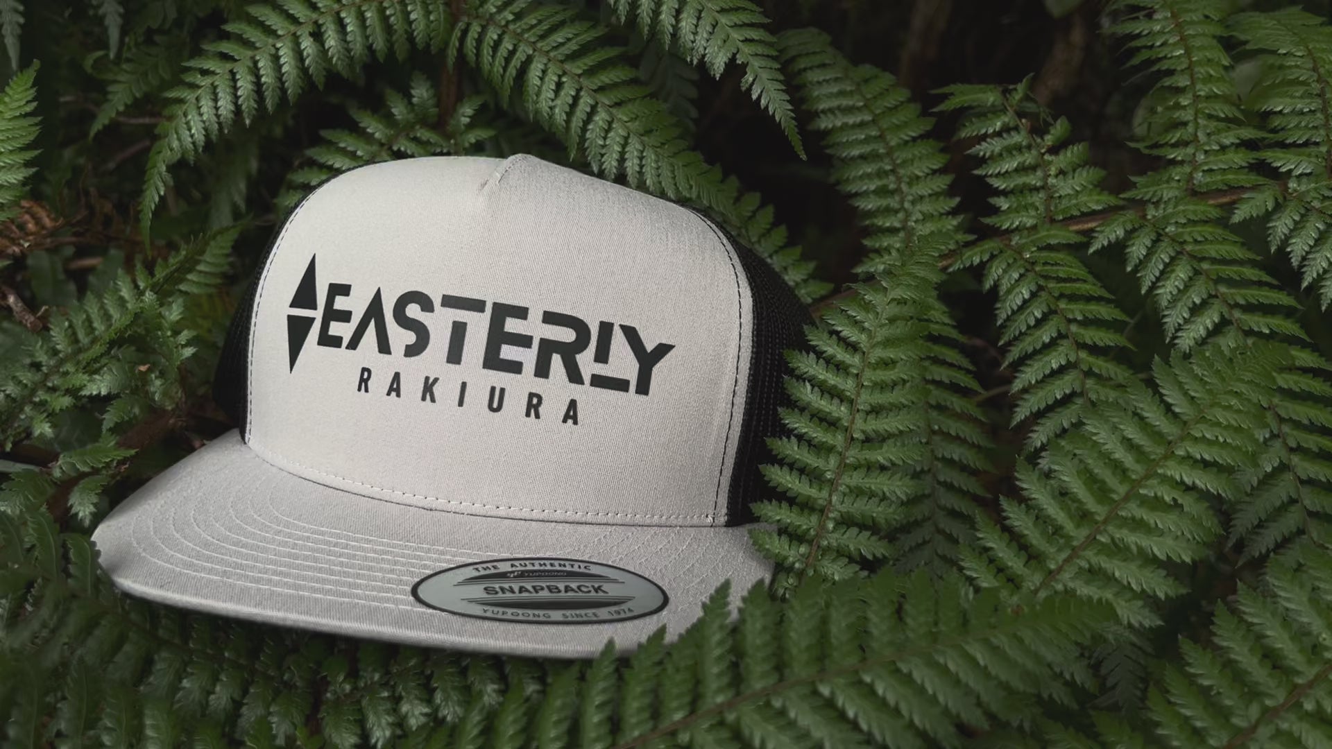 EASTERLY Rakiura trucker cap in stone — recycled snapback hat resting on a native fern with New Zealand birdsong, Stewart Island NZ